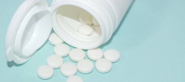 Açık beyaz plastik kavanoz, açık mavi arka planda beyaz dağınık haplar, tıp konsepti, boşluğun kopyası, afiş.