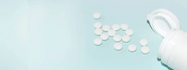 White open plastic jar with a bunch of white scattered pills on a light blue background, medicine concept, copy of the space, banner