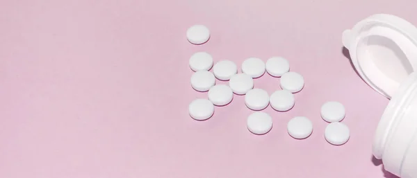 En hög med piller låg framför en öppen liten plastflaska på en ljusrosa bakgrund, en banner — Stockfoto