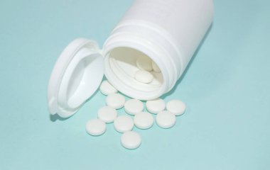 Açık küçük bir plastik şişenin önünde açık mavi bir zemin üzerinde bir yığın hap vardı.