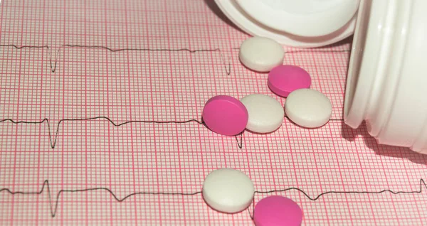 심장병 예방 개념 인종이 심전도에 알약이 붙어 있는 병에서 흘러나오는 캡슐들 — 스톡 사진