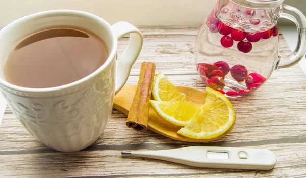 A Cup of hot tea, lemon, cinnamon, a jug of cranberry drink. The concept of treating colds — Stock Photo, Image