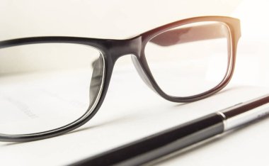 Lüks erkek aksesuarları, şık siyah gözlükler ve beyaz bir masaüstü arka planında bir kalem. Ofisin içinde hiç kimse yok.