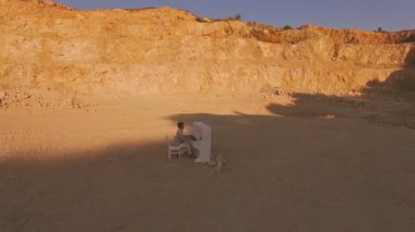 Genç adam sarı cliff bir arka plan üzerinde beyaz bir piyano üzerinde çalış. Havadan görünümü