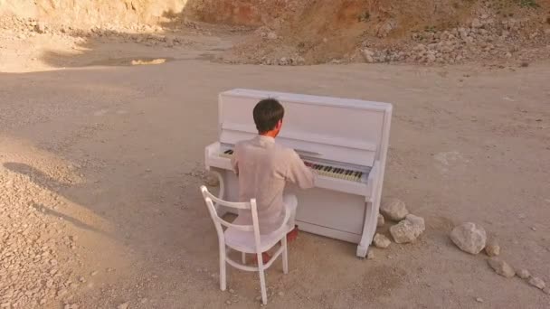 Young man plays the piano on a background of yellow mountains and stones — Stock Video