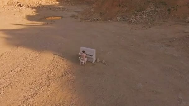 Joven toca el piano sobre un fondo de montañas amarillas y piedras. concierto fantástico — Vídeos de Stock