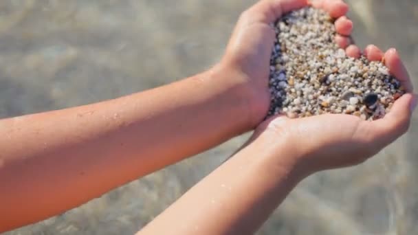 La niña sostiene un corazón de arena marina en el fondo contra el agua transparente del mar. El concepto de unas vacaciones románticas de verano — Vídeos de Stock