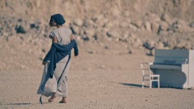 Yorgun genç kadın çıplak ayakla çakıl dağlar ve beyaz piyano arka plan üzerinde yürür