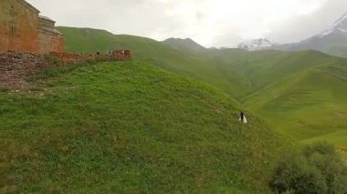 Mutlu gelin ve damat dağlar ve eski kilisenin arka planda. Gürcistan. havadan görünümü
