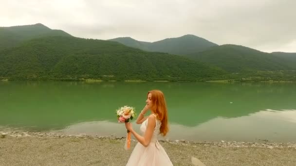 Noiva bonita e feliz e noivo na margem do rio. A noiva lança um buquê de casamento — Vídeo de Stock