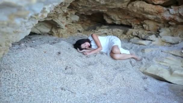 Frightened girl lies on the sand in a stone grotto and the tide of the sea approaches her — Stock Video
