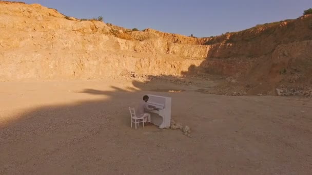 Jeune homme joue sur un piano blanc sur un fond de falaise jaune. Vue aérienne — Video