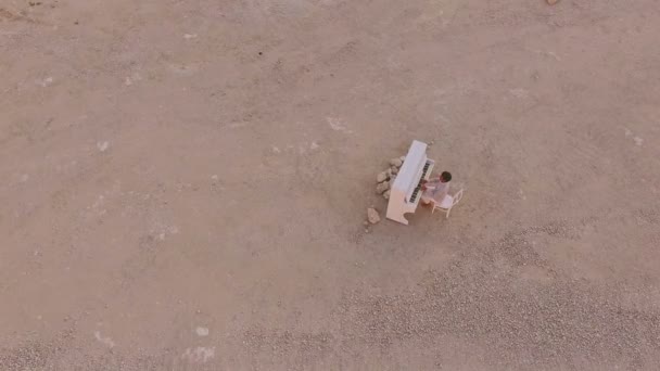 若い男は、黄色の崖の背景に白いピアノを果たしています。航空写真ビュー — ストック動画