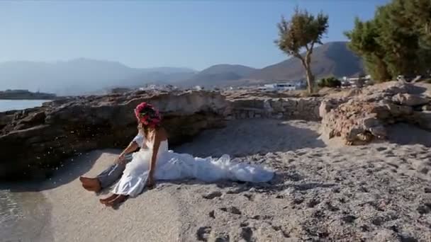 Счастливые и веселые жених и невеста сидят на пляже в день своей свадьбы — стоковое видео