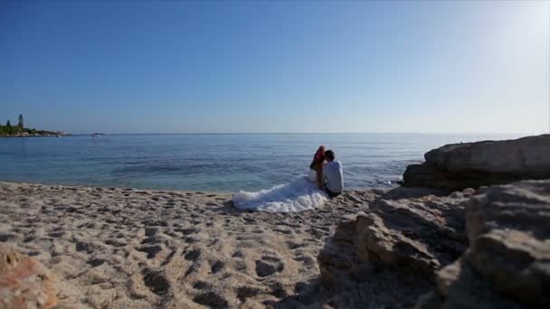 Happy and cheerful bride and groom are sitting on the beach on their wedding day — Stock Video