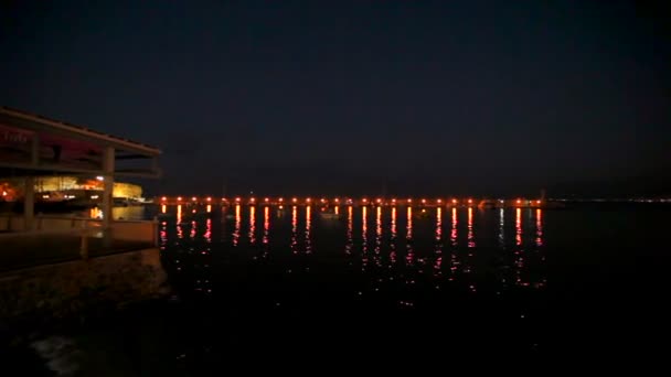 Starkt ljus återspeglas i det mörka havet vattnet på bryggan med båtar. bokeh. — Stockvideo