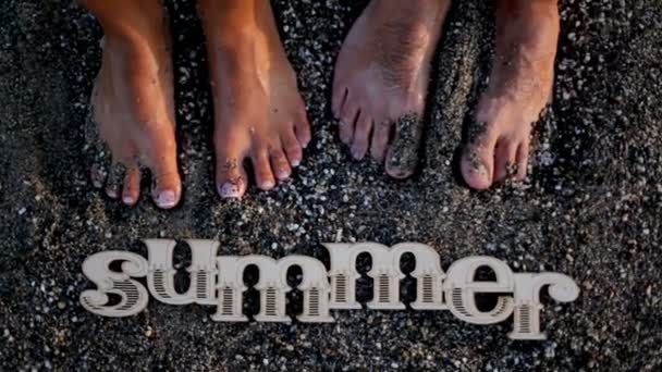Romántico chico y chica están de pie en la arena mojada de la playa cerca de la palabra verano — Vídeos de Stock