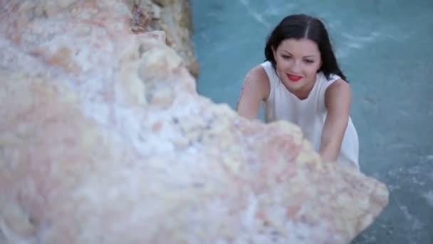 Beautiful brunette girl walking on steep stone beach — Stock Video