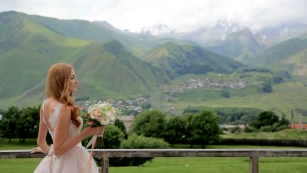 美しい花嫁は、美しい山の風景と花の花束を楽しんでいます。結婚式の日 — ストック動画