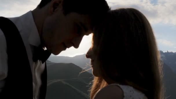 Sziluettjét a lenyugvó nap, a hegyek a háttérben egy szerető pár. — Stock videók