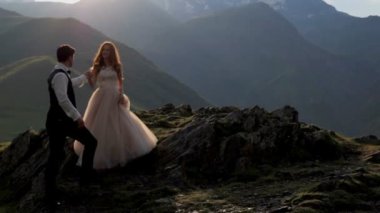 Bir muhteşem gelin ve damat görkemli dağlarda yaz gün batımında arka planı. Gürcistan. Mutlu bir aile hayatı kavramı