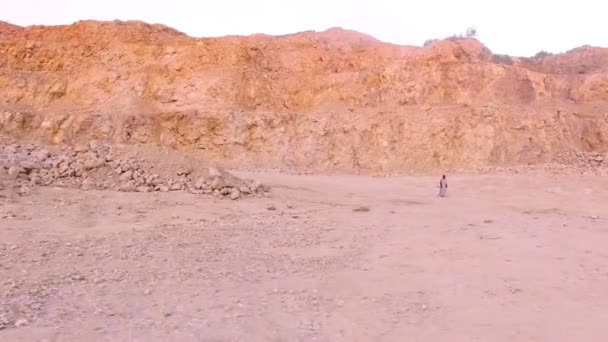 Одинокая молодая женщина, идущая босиком по песку на фоне гор. Вид с воздуха — стоковое видео