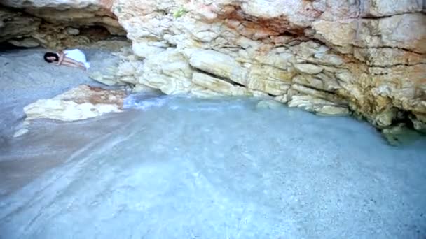 En skrämd flicka ligger på sanden i en sten grotta — Stockvideo