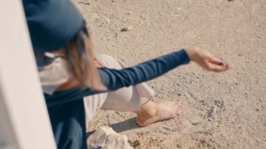 Deli bir genç kadının çölde bir beyaz piyano yakınındaki kayalarda oturur ve kum dökülen