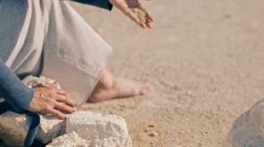 Deli bir genç kadının çölde bir beyaz piyano yakınındaki kayalarda oturur ve kum dökülen