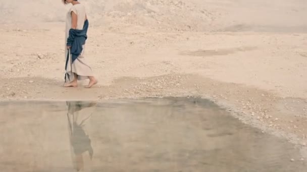 Молодая женщина идет вдоль берега озера на фоне горы и тумана — стоковое видео