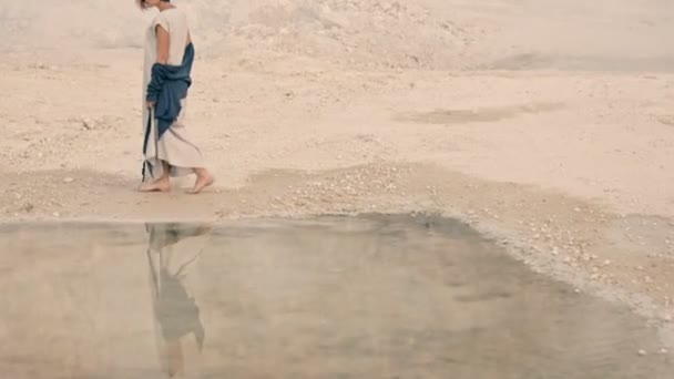 Joven mujer va a lo largo de la orilla del lago contra el telón de fondo de la montaña y la niebla — Vídeo de stock