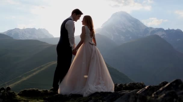 Zamilovaný novomanželé mají velikou radost krásný letní večer v paprscích zapadajícího slunce na pozadí majestátní hory. Koncept šťastný rodinný život — Stock video
