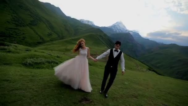 Zamilovaný novomanželé chodit večer na louce na pozadí hory. — Stock video