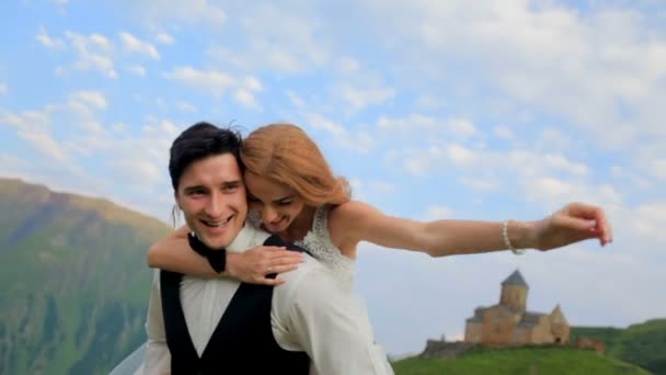 La novia y el novio se divierten el día de su boda en medio de las majestuosas montañas, la antigua iglesia en un día soleado de verano. Georgia — Vídeos de Stock