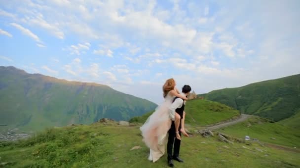 新娘和新郎在他们的婚礼当天在雄伟的山脉 古老的教堂和蓝天与白云在一个夏日晴朗的一天的乐趣 格鲁吉亚 — 图库视频影像