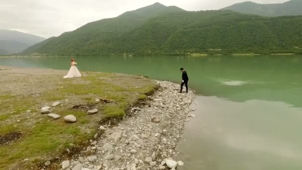 Luchtfoto. Bruid en bruidegom op de achtergrond van de rivier en de bergen. — Stockvideo