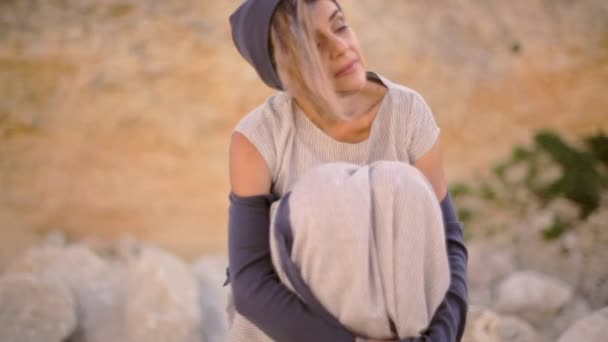Een eenzame jonge barefoot vrouw zit op een grote steen in de buurt van de berg. — Stockvideo
