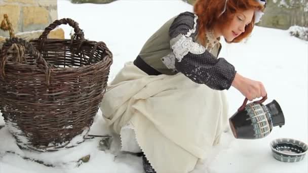 Krásná rusovlasá dívka v etnické oblečení nalévá mléko pro psa v talířek