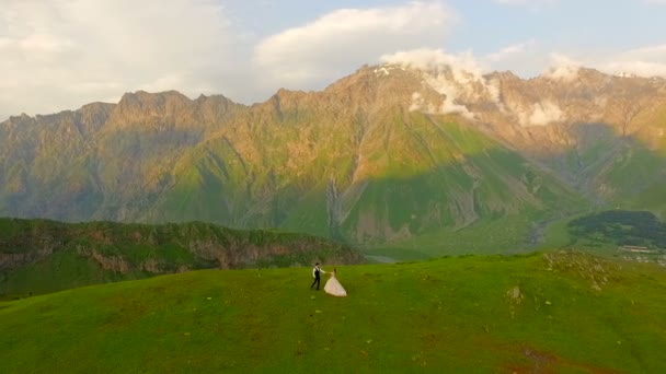 Зачаровані молодята гуляють увечері на лузі на тлі красивих гір — стокове відео