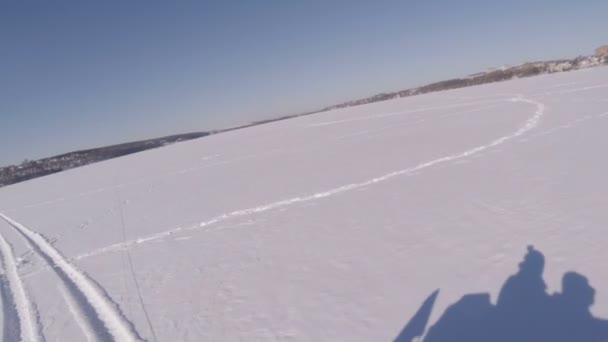 Два парня едут на снегоходе по замерзшему озеру. Тени парней в снегу — стоковое видео