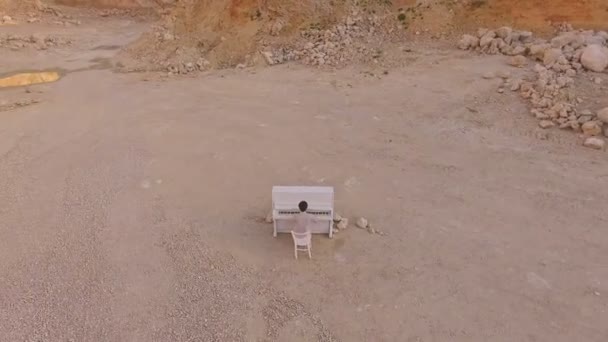 Un joven toca un piano blanco sobre un fondo de acantilado amarillo. Vista aérea. Surrealismo — Vídeos de Stock