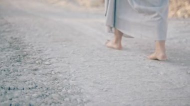 uzun elbiseli kadın çıplak ayakla kumlu yolda yürür. Gövde bölümü