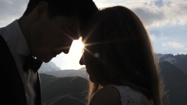 Novomanželé v lásce polibek v paprscích zapadajícího slunce vysokou v horách — Stock video