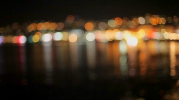 Helle Lichter spiegeln sich im dunklen Meerwasser an der Seebrücke mit ihren Booten. Bokeh. — Stockvideo