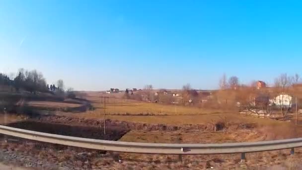 Arbres sans feuilles, champs et ciel bleu scintillant devant la fenêtre d'une voiture en mouvement — Video