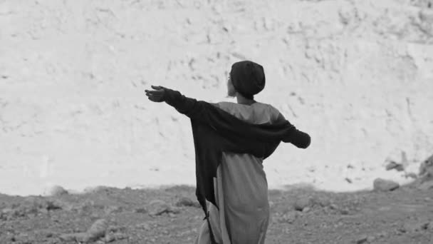 女孩在岩石附近的沙漠里跳着一种仪式的舞蹈。黑白图像 — 图库视频影像