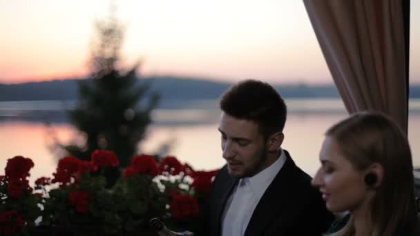 Dos rubias llegaron en una cita romántica con dos chicos en un café de verano en la terraza al aire libre con vistas al lago . — Vídeos de Stock