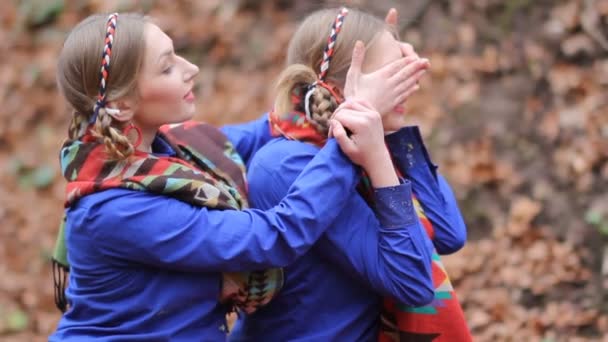 Dos niñas gemelas alegres están sentadas en el bosque de otoño entre el follaje amarillo caído . — Vídeos de Stock