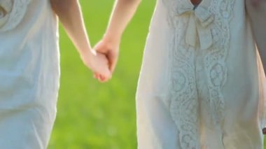 Beyaz keten elbiseler iki kız Twins güneşli bir günde kırsal yeşil bir çayır boyunca yürümek. Vücut parçaları