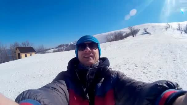 Jovem cara feliz leva uma selfie nas montanhas nevadas contra o pano de fundo de uma paisagem de inverno deslumbrante . — Vídeo de Stock